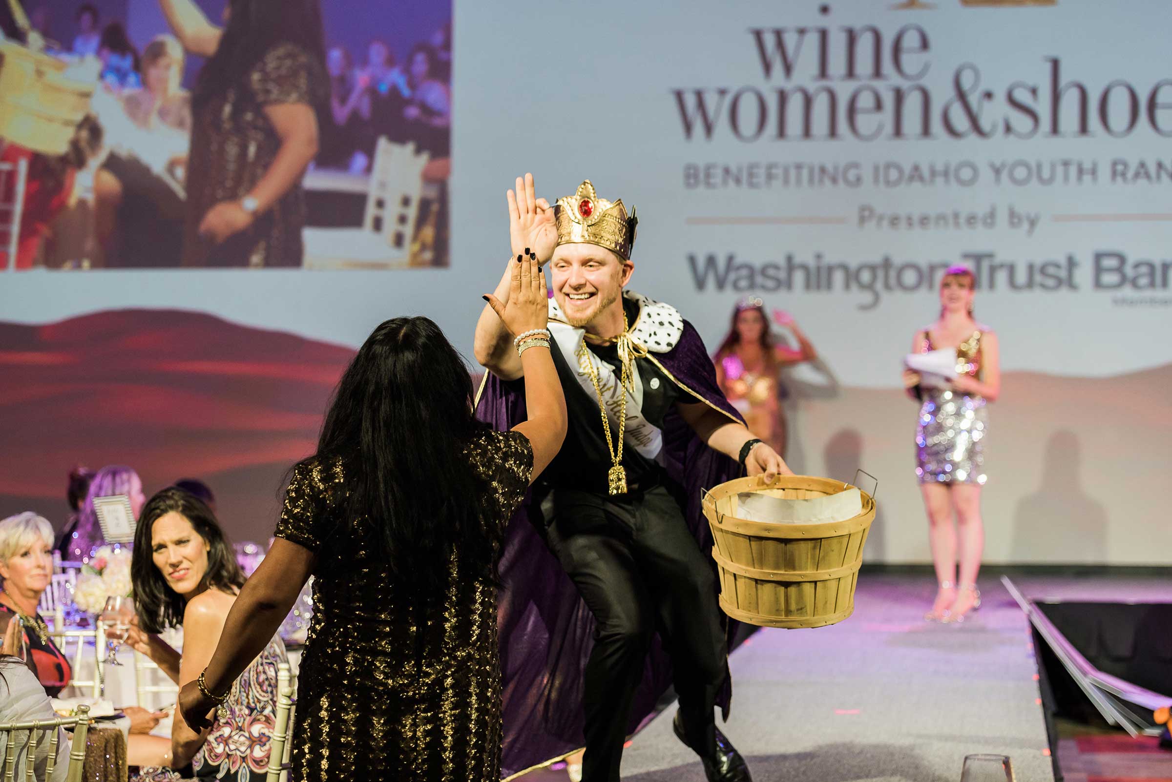 man on a stage dressed in king costume high fives a woman in the audience